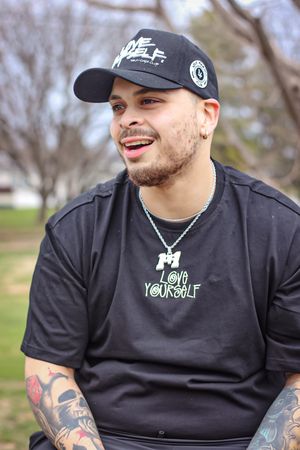 Lifestyle shots of person wearing branded black t-shirt and cap in park setting.