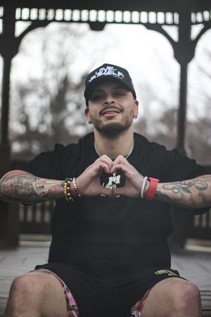 Tattooed person in black shirt and baseball cap seated outdoors showing various poses.