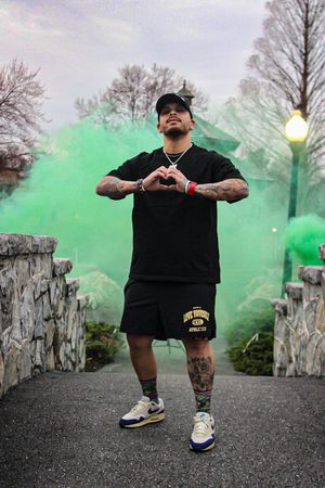 Person in black shirt poses with green smoke effects in urban setting.