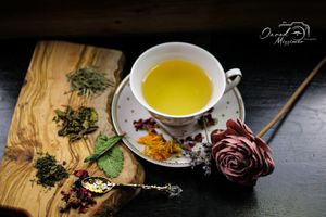 Yellow tea in vintage cup with dried herbs and red rose on wooden surface.