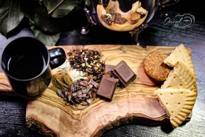Cozy tea arrangement with chocolate, biscuits and dried fruits on wooden serving board.