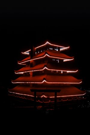 Illuminated red pagoda temple glowing against dark night sky.