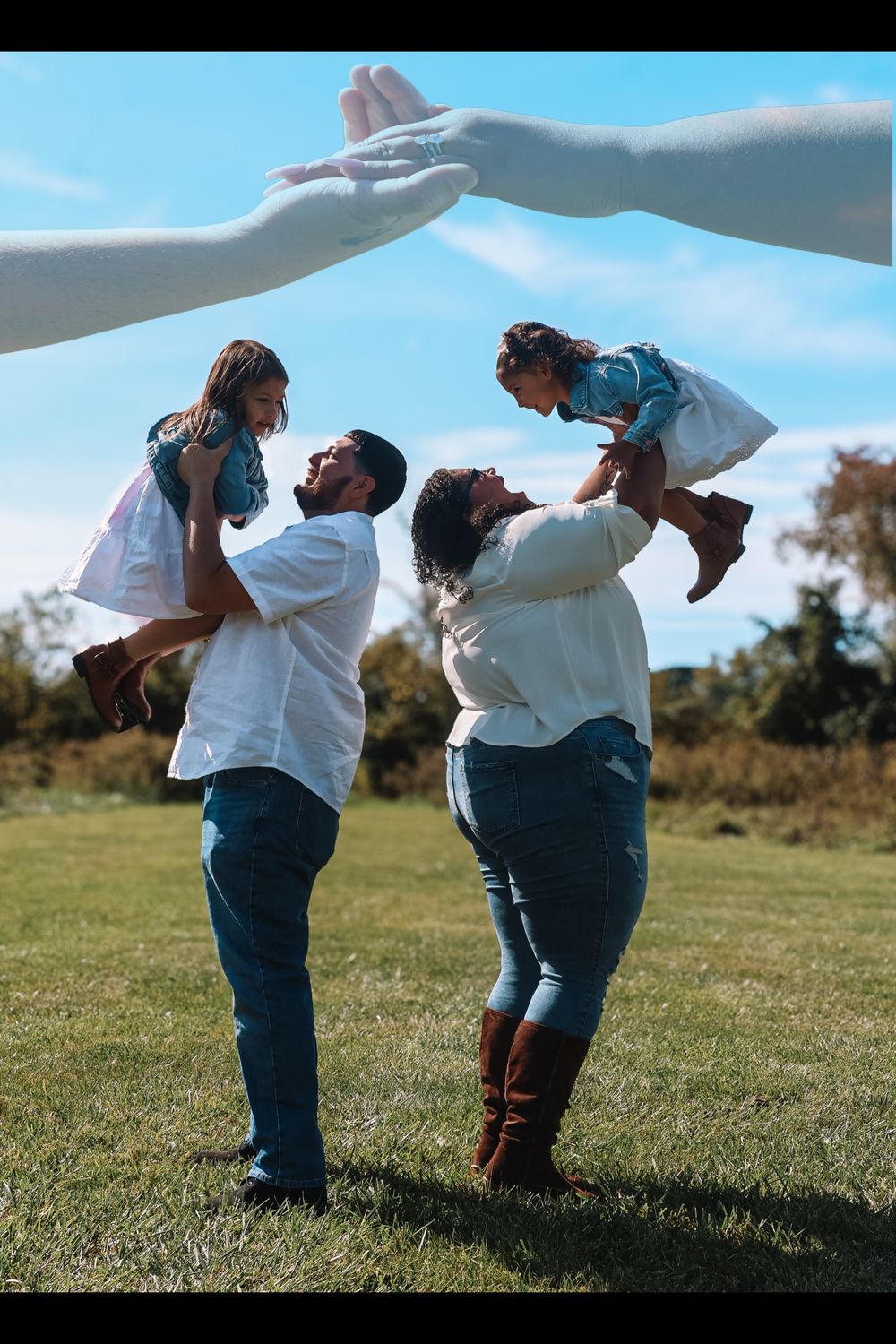 A family plays together outdoors on a sunny day, lifting children up against a bright blue sky in a grassy field.