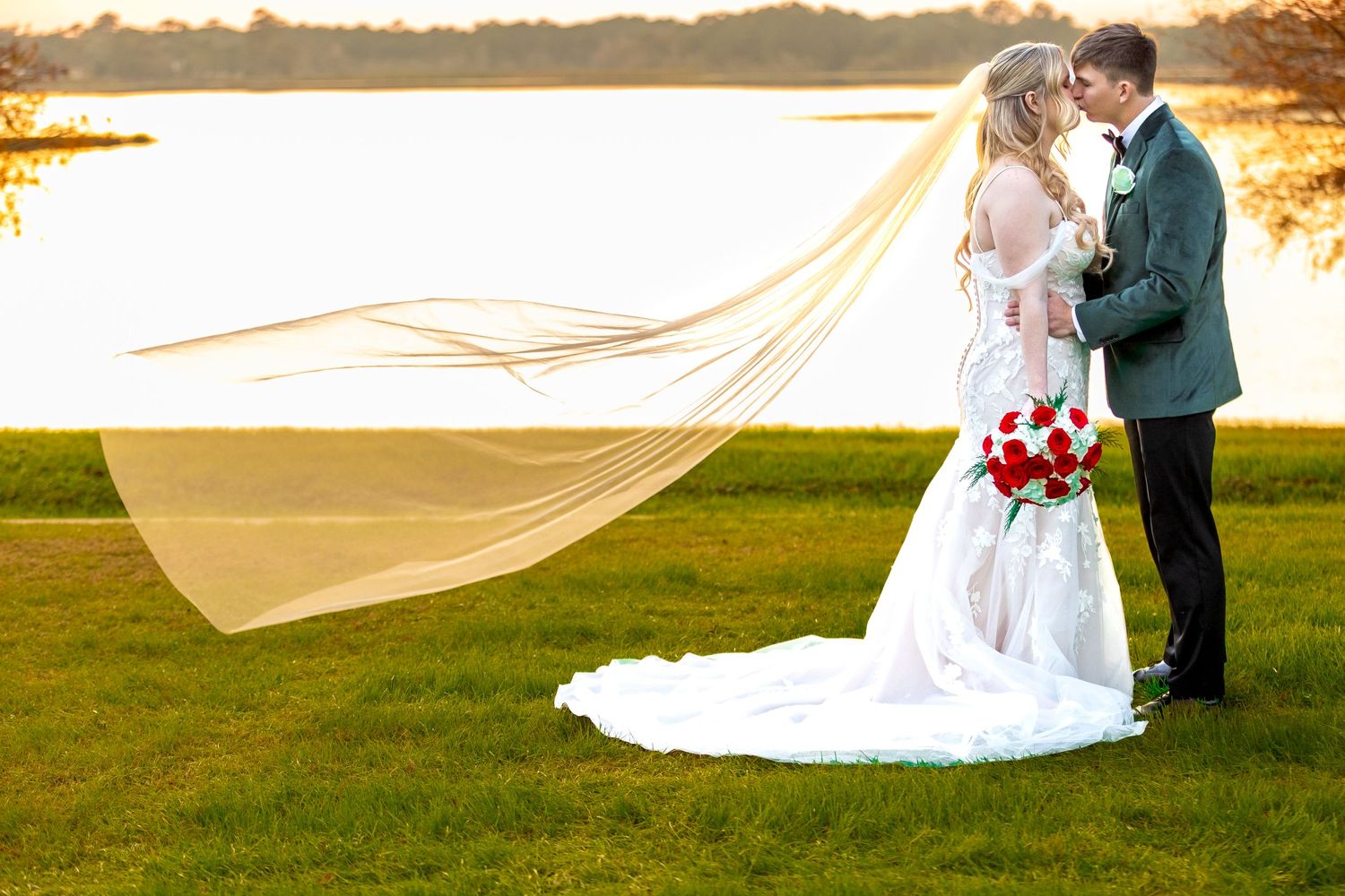 A romantic sunset wedding photo with a flowing veil and red bouquet by a lake. Lake Mary, Florida
