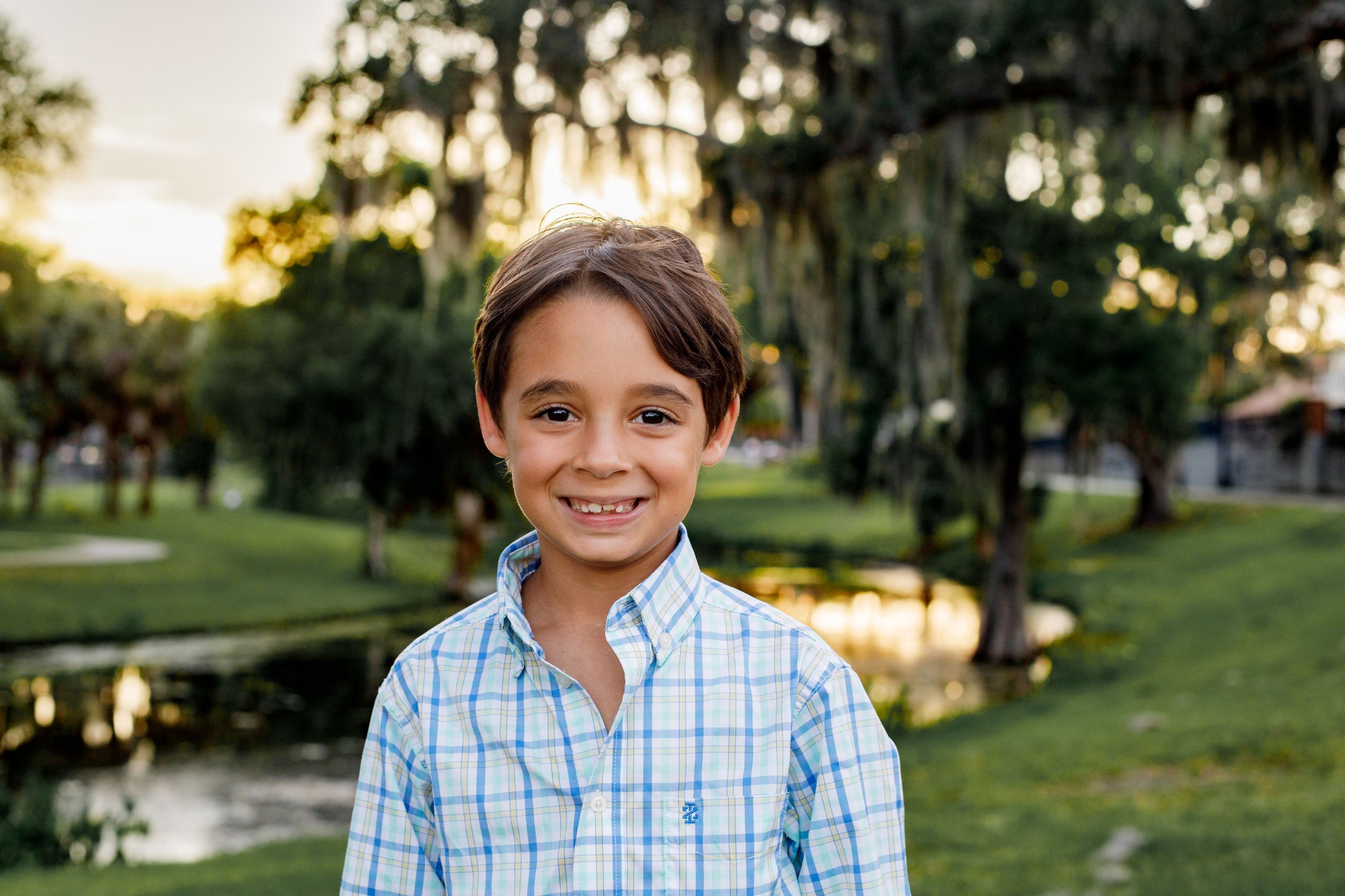 Child in blue checkered shirt smiling outdoors during golden hour.