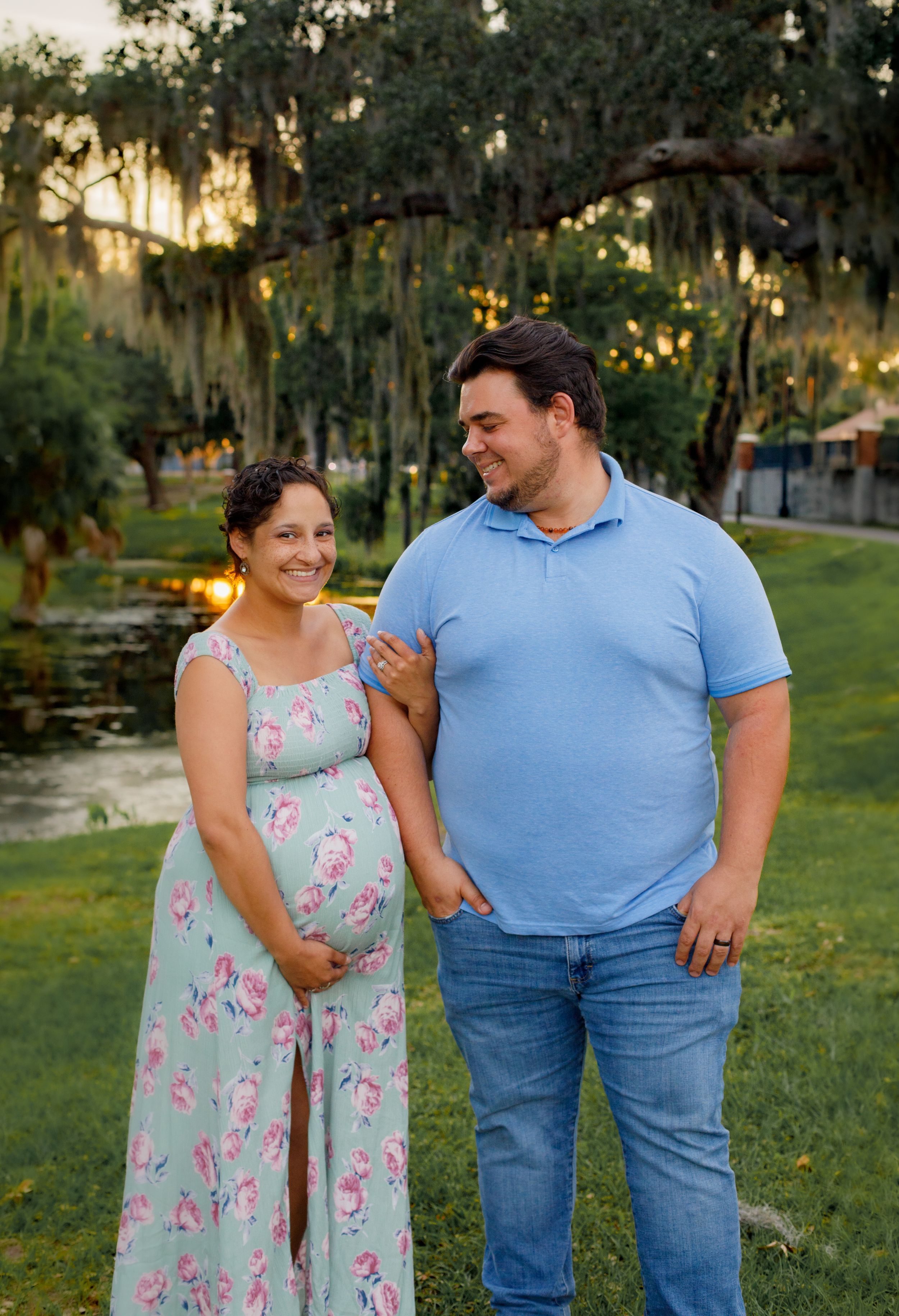Couple poses together outdoors, woman wearing mint floral dress and man in blue shirt.