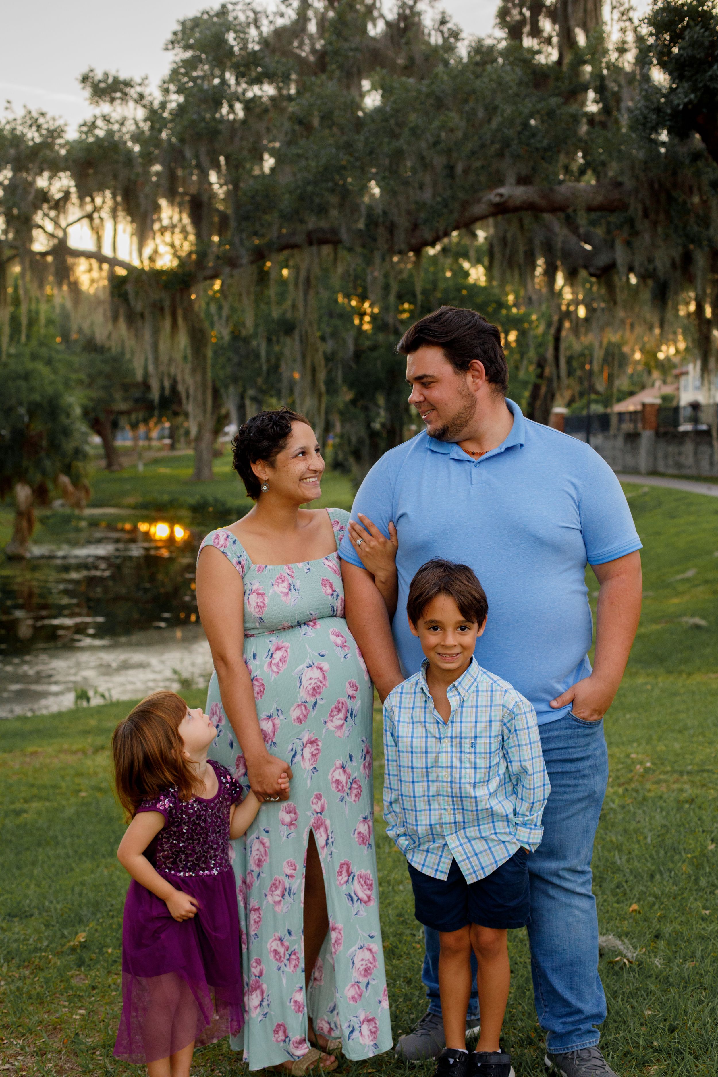 Family stands together in a park with Spanish moss trees during golden hour.