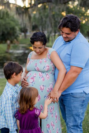 Family gathering outdoors at sunset with a pregnant woman in a floral dress.