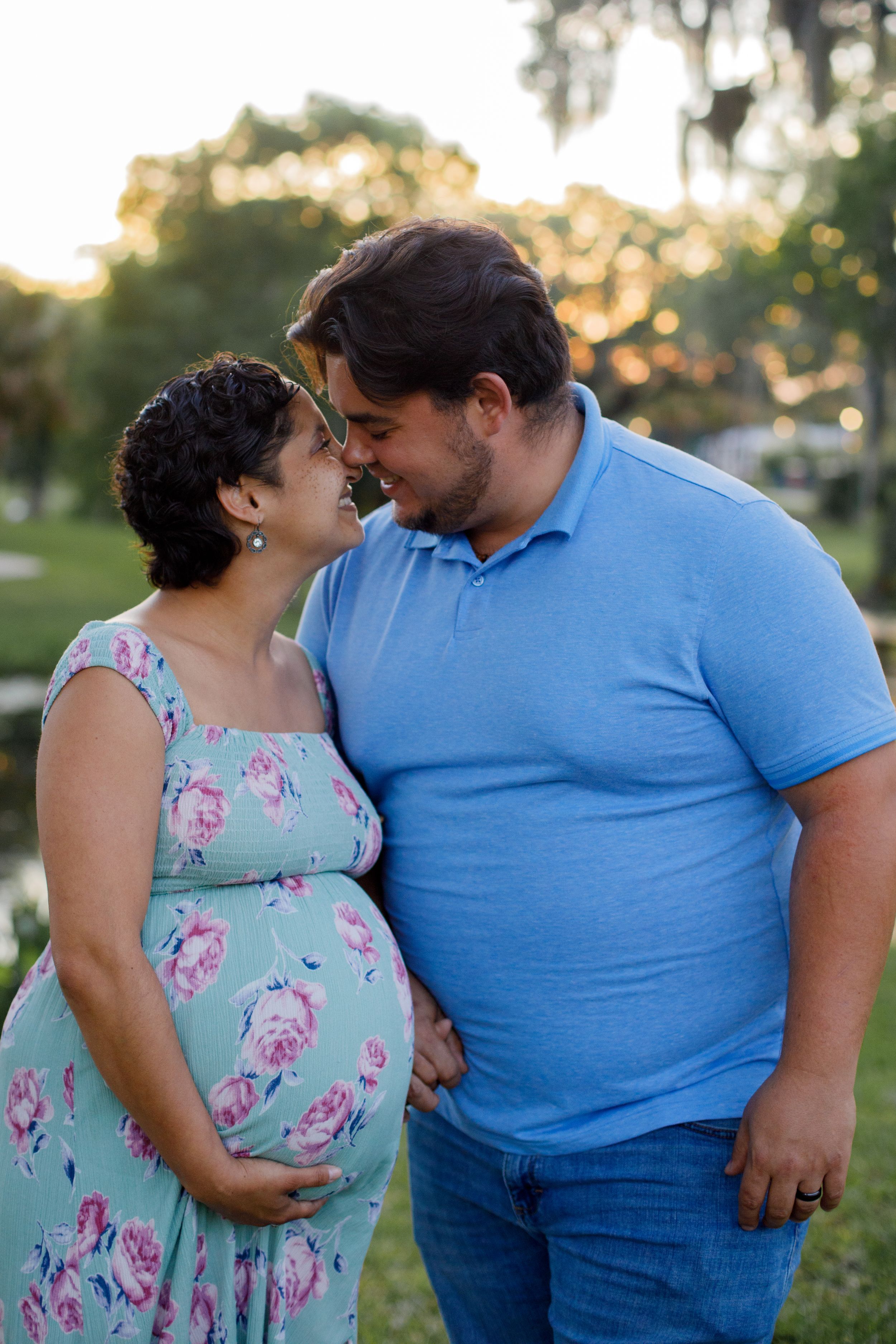 Intimate couple portrait outdoors with woman in floral dress and man in blue shirt.