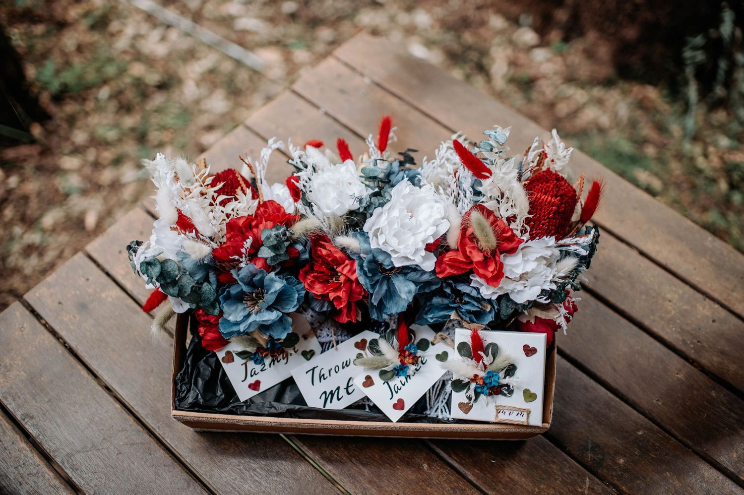 A wooden box filled with red and blue wedding favors and decorative elements.