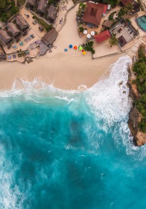 Aerial view of a tropical beach resort with turquoise waters crashing onto sandy shores and colorful umbrellas.
