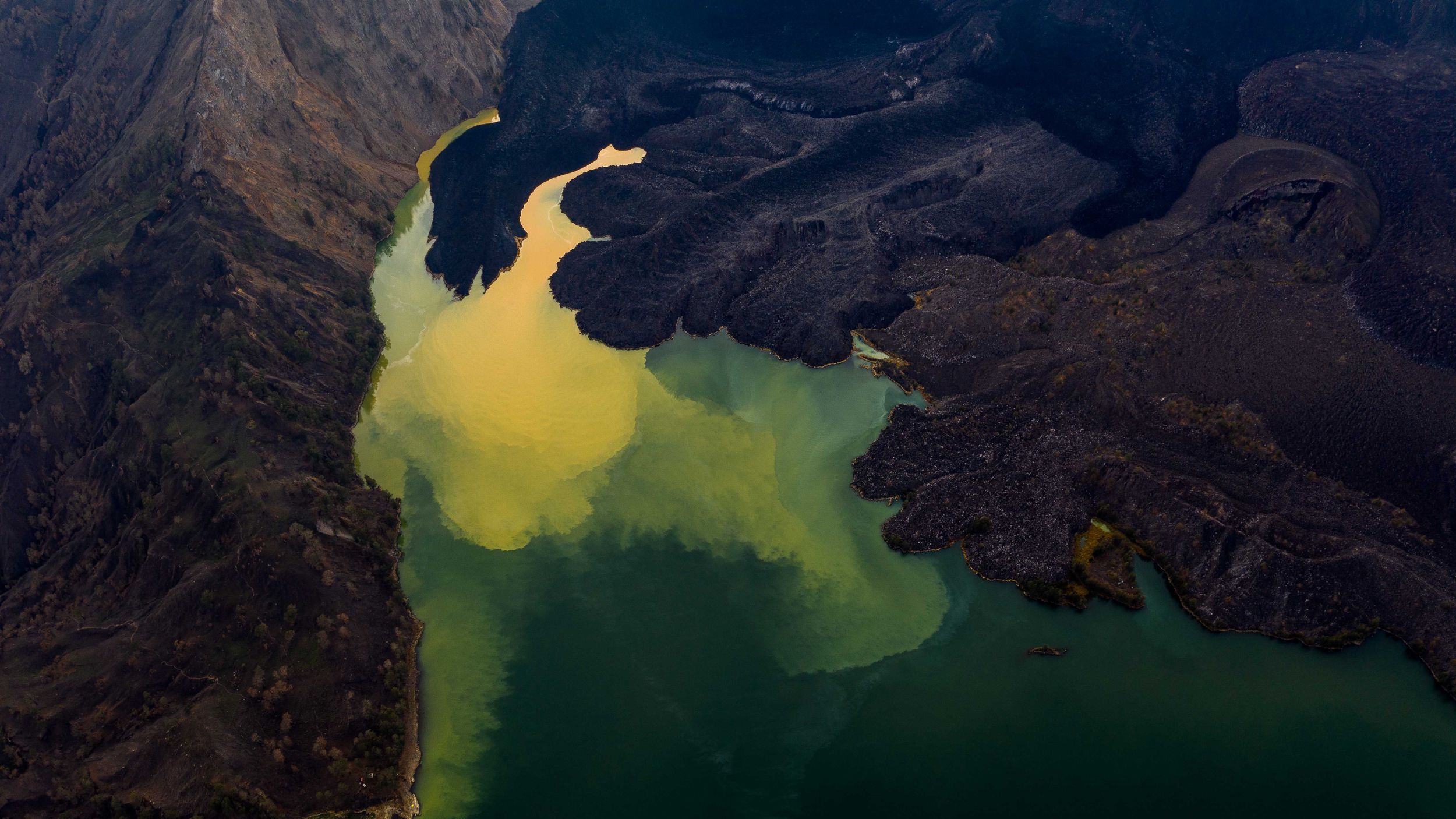 Aerial view of a winding river with yellow and green water flowing through mountainous terrain.