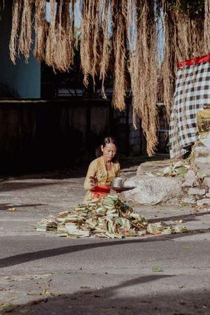 Traditional artisan working with dried natural fibers under hanging materials in Bali.