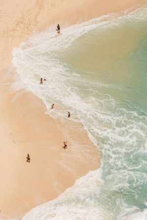 Bird's eye view of people walking along pristine beach where turquoise waves meet golden sand.