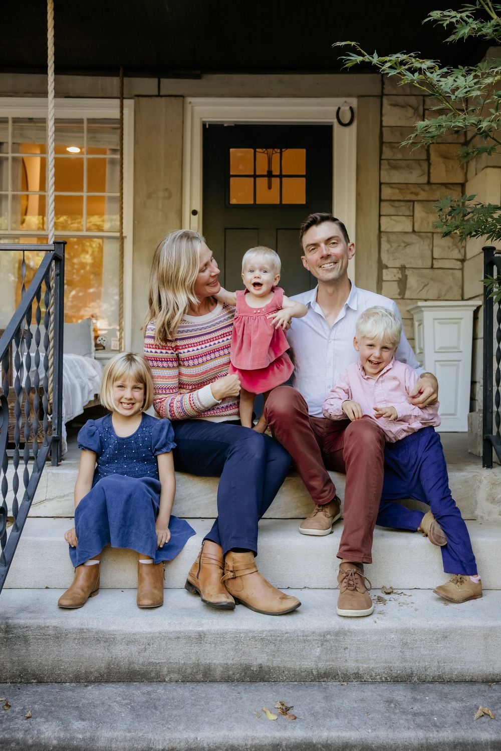 A family sits together on stone steps outside their home wearing coordinated casual outfits in blue and pink tones.