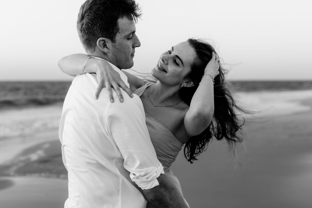 Black and white portrait of dancing couple on beach at sunset.