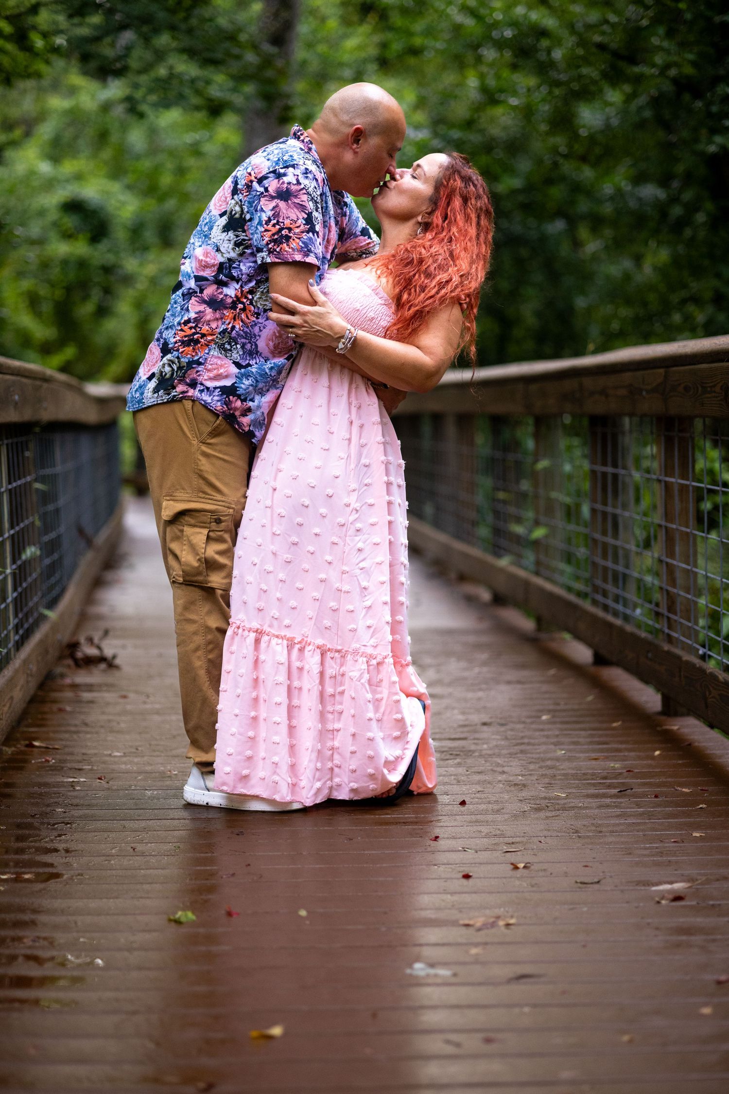 A couple shares a romantic moment on a wooden bridge surrounded by lush greenery. Oviedo, Florida