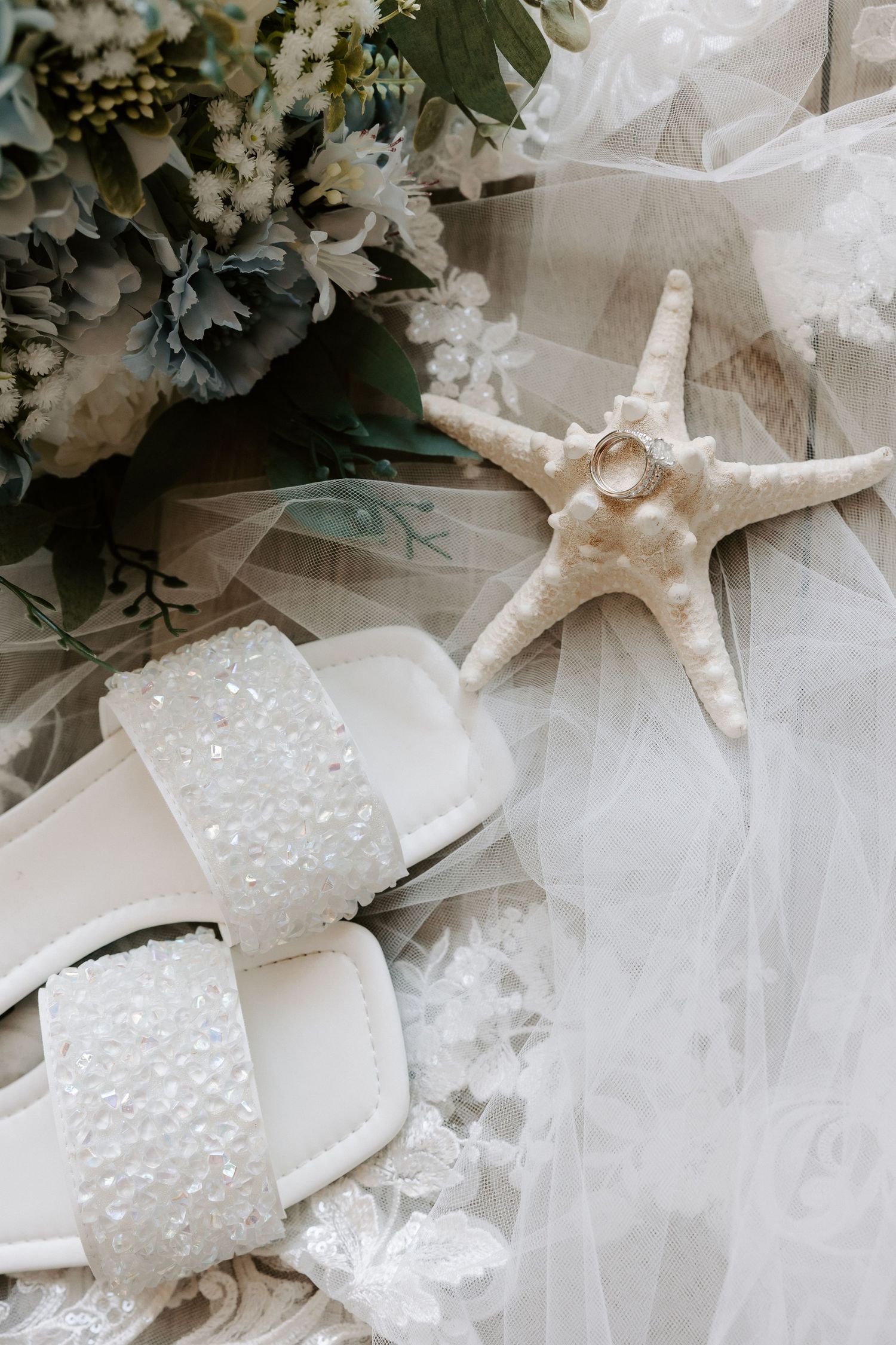 Wedding details featuring a starfish, pearl-embellished shoes, and white flowers on tulle fabric.