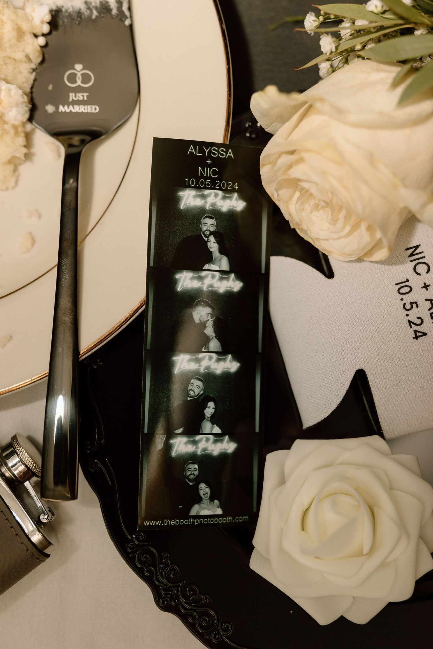 Wedding details with black serving utensils, white roses and photo strip on dark surface.