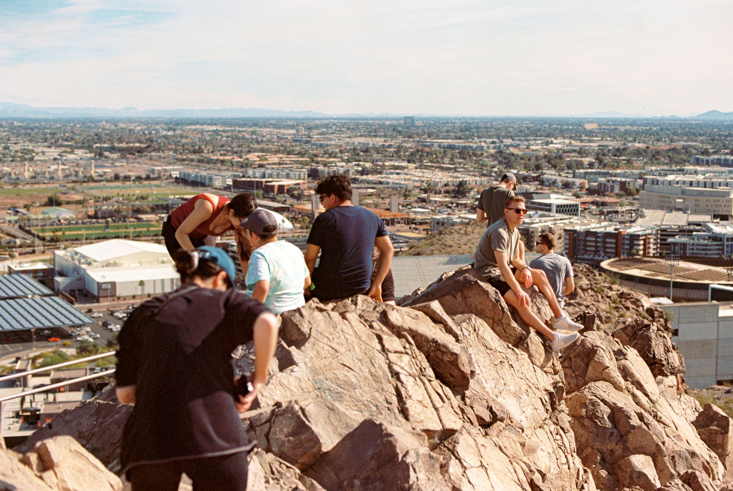 Panoramic view of people gathered on a rocky overlook above a sprawling city.