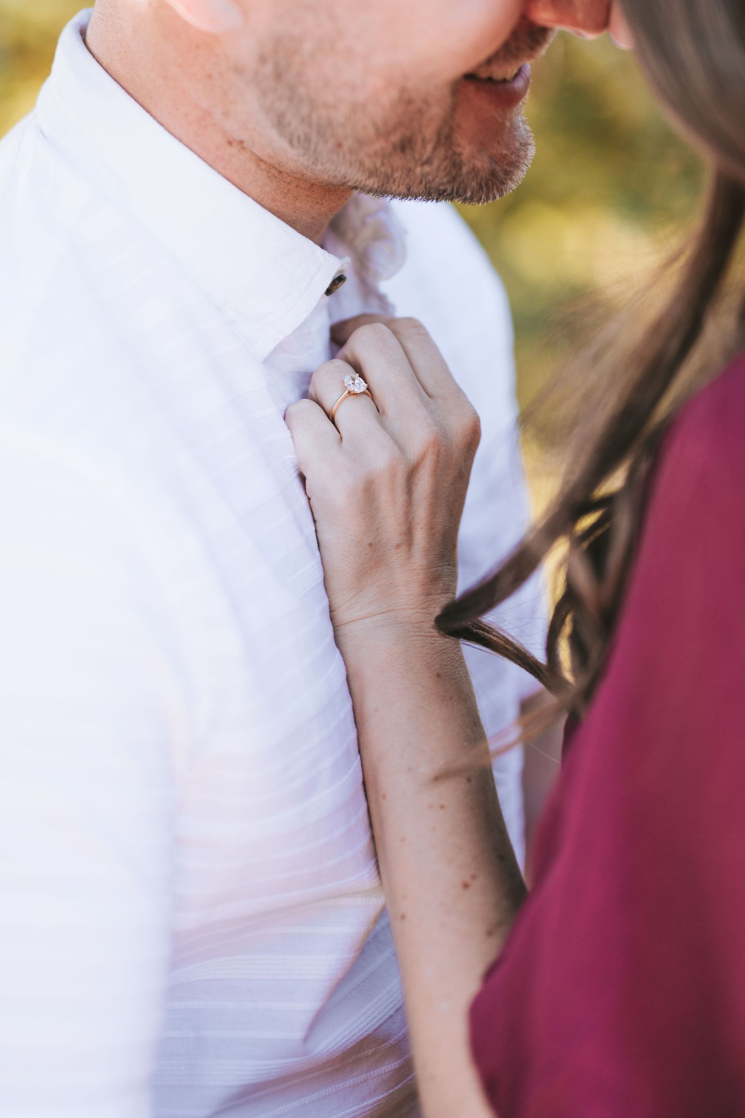 Close-up of a hand gently adjusting a white collar shirt showing an engagement ring.