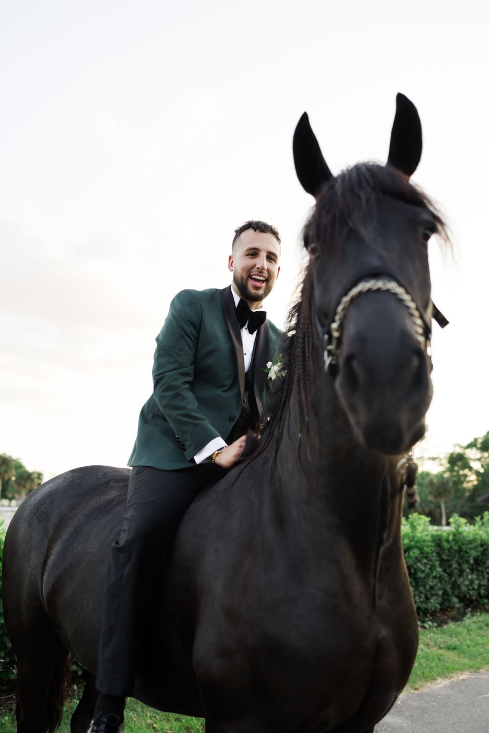 Person in emerald tuxedo shares a joyful moment with a black horse during wedding photography.