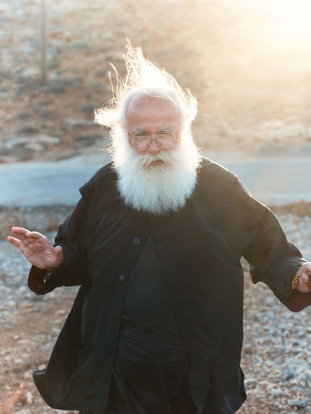 Orthodox clergy member in black robes gestures dramatically in golden sunlight.