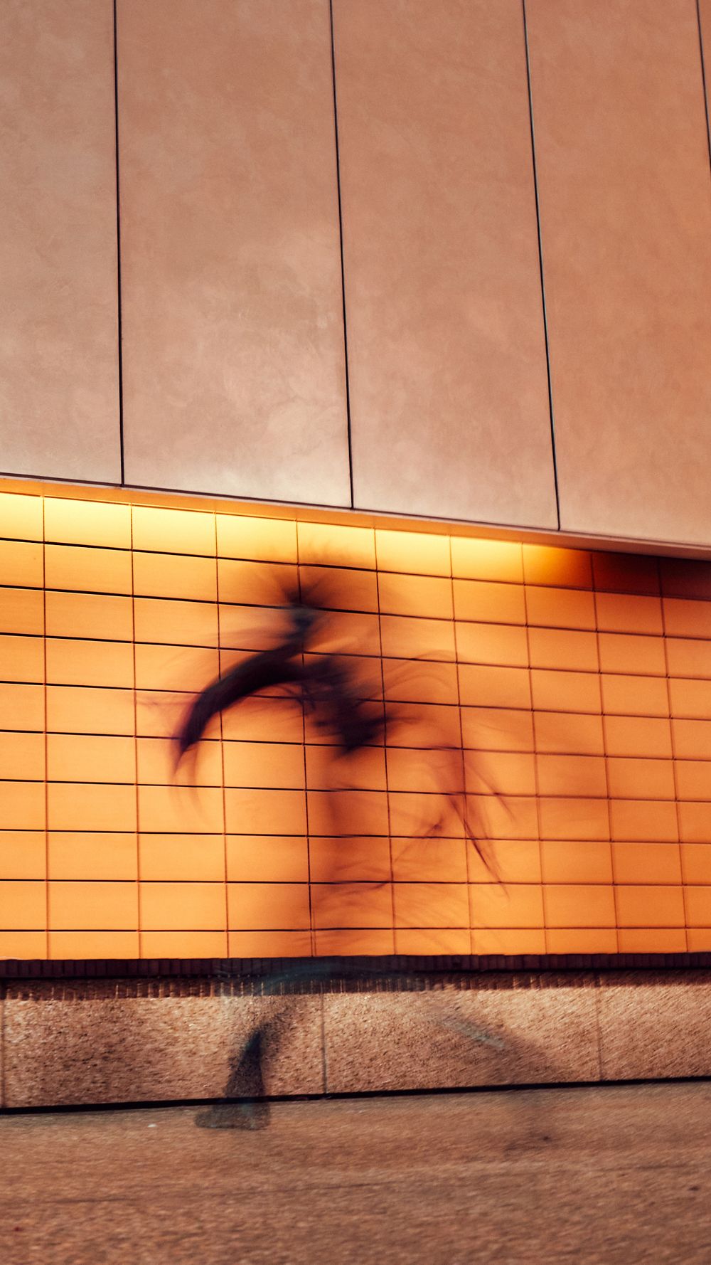 Sunset creates dramatic shadows on orange-tinted tiled wall with linear patterns.