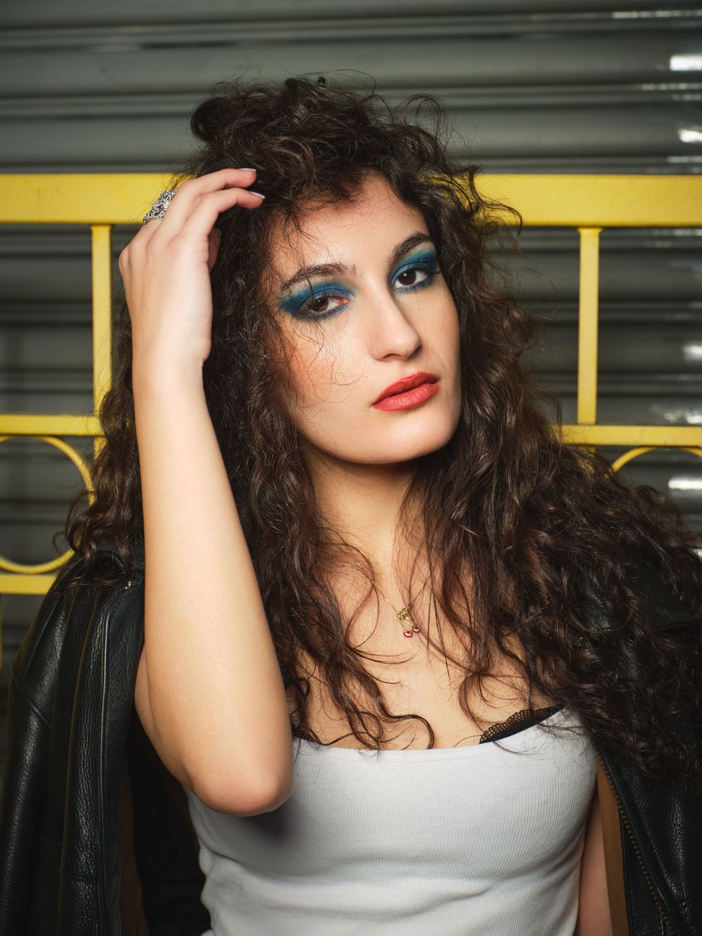 Fashion portrait of a woman with dramatic curly hair and bold blue eyeshadow in a parking garage setting.
