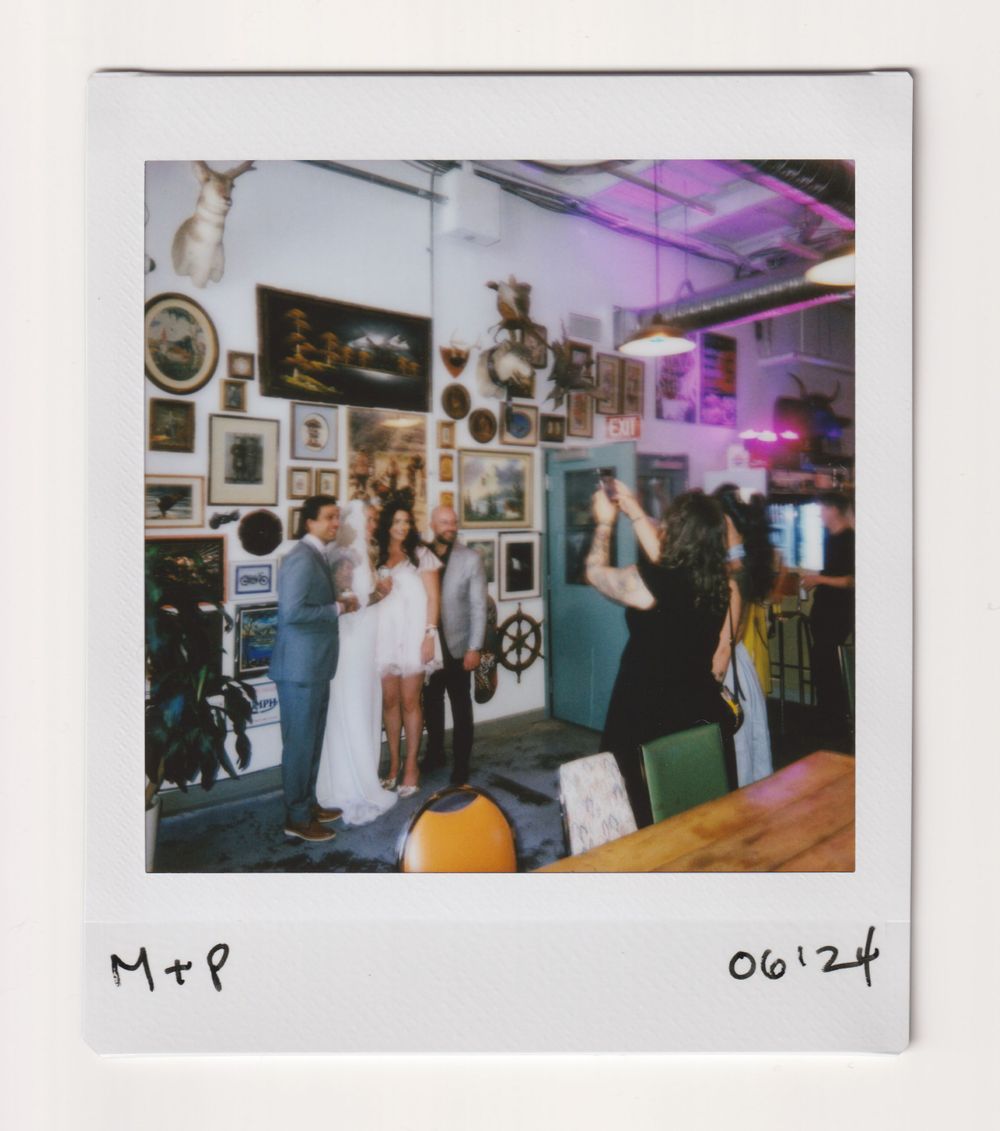Interior of an eclectic venue with artwork-covered walls and partygoers under purple lighting.