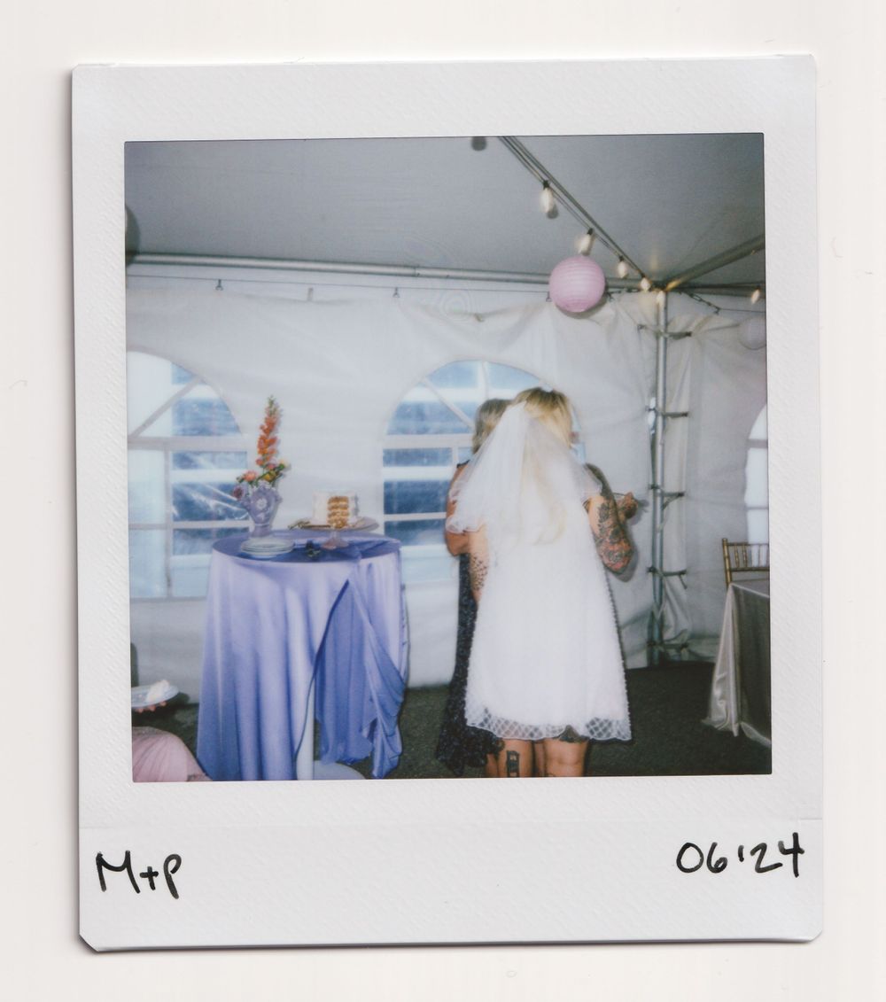 Reception setup with blue tablecloth and white dress visible in tent setting with paper lanterns.