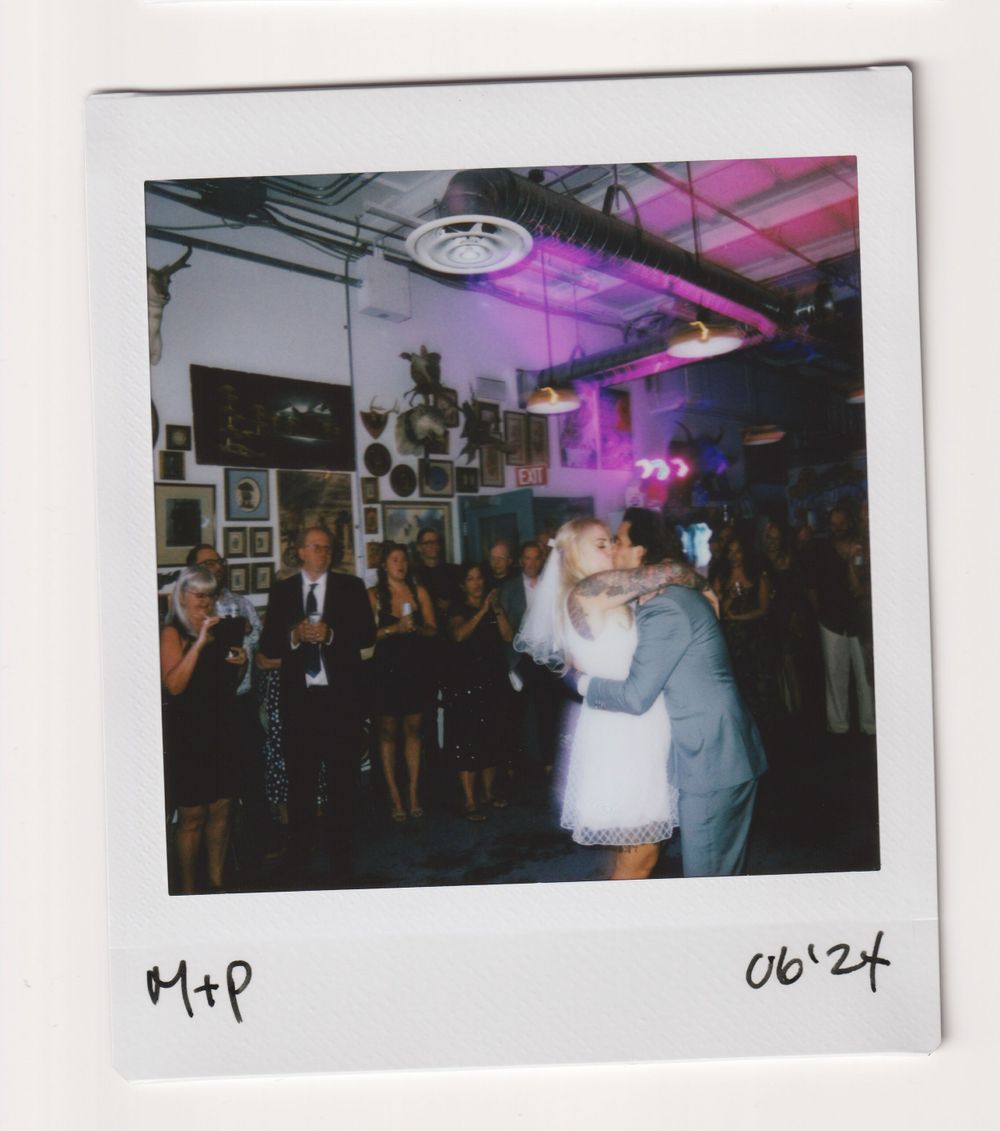 A couple dancing at their wedding reception under purple mood lighting in an industrial-style venue.