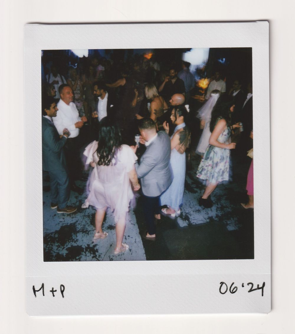 Large group of people dancing at a nighttime celebration captured in vintage polaroid style.