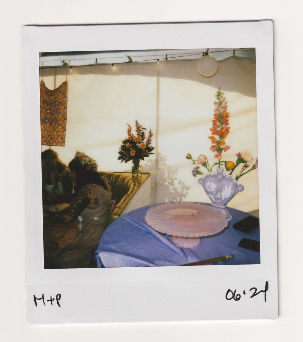 Table setting with purple tablecloth and floral centerpiece in vase under tent lighting.