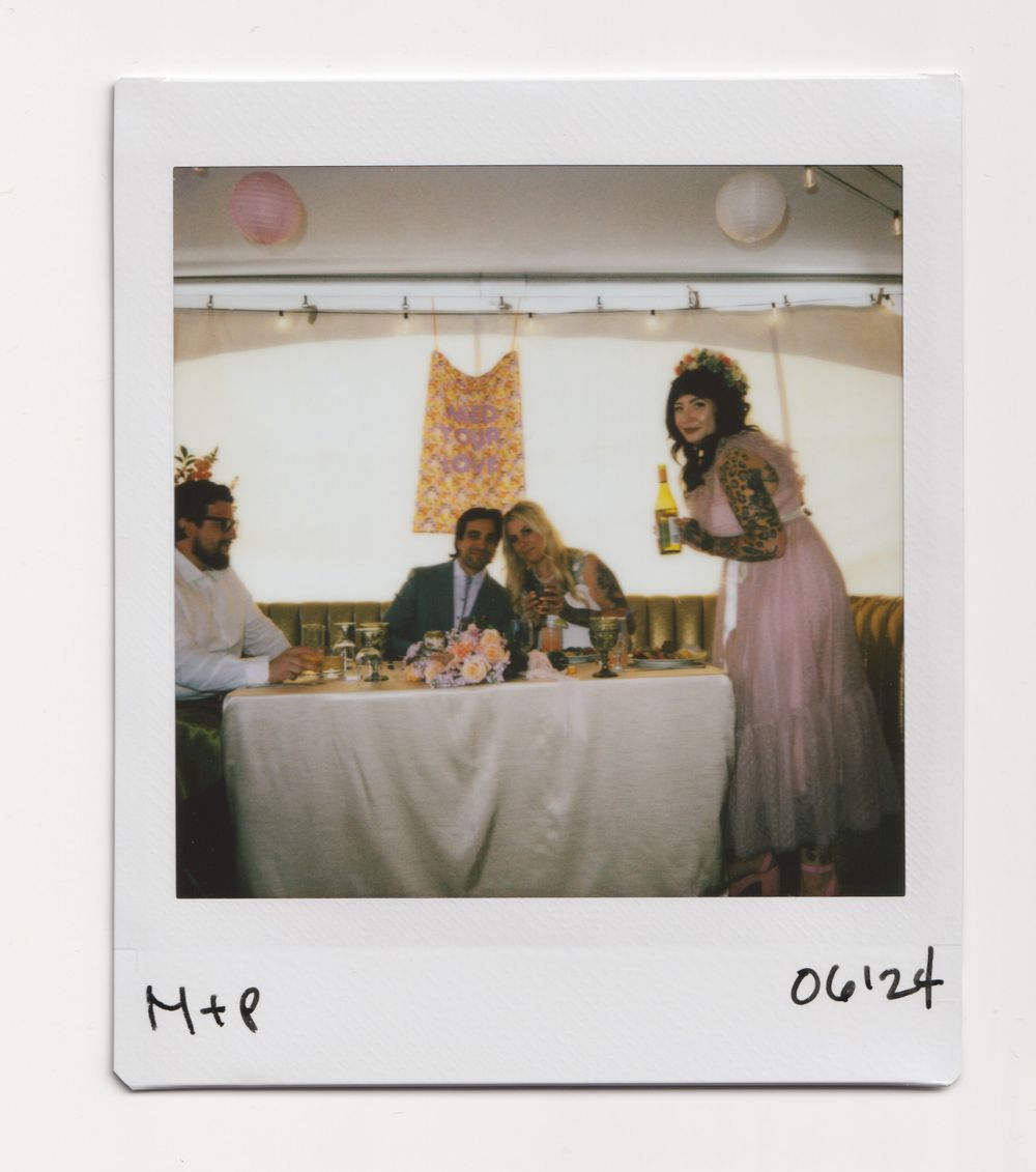 Wedding reception scene with guests at decorated head table under white tent ceiling.