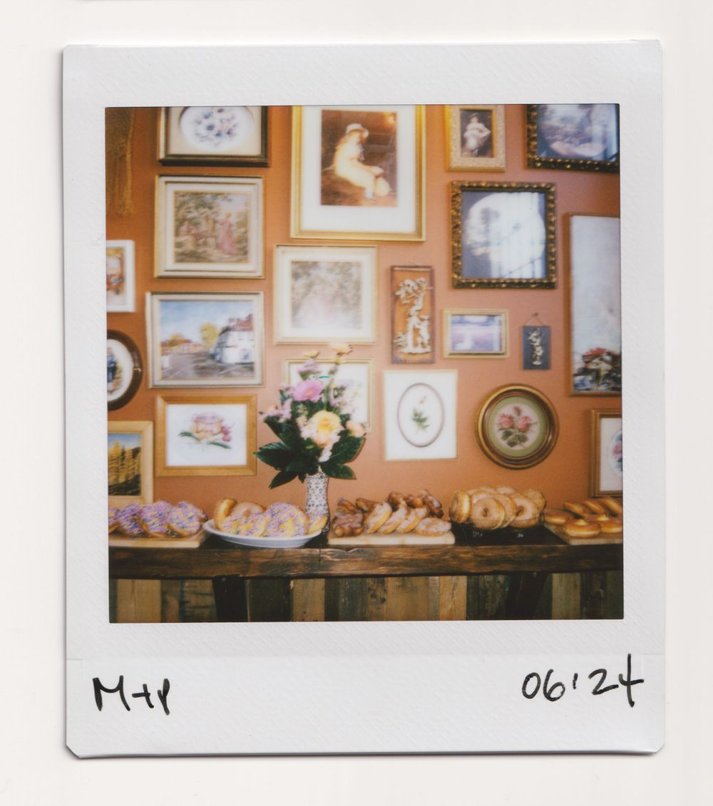 Gallery wall with framed artwork and photos above table with flower arrangement and pastries.
