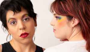 Two people with colorful Pride-themed makeup pose together in an artistic portrait.