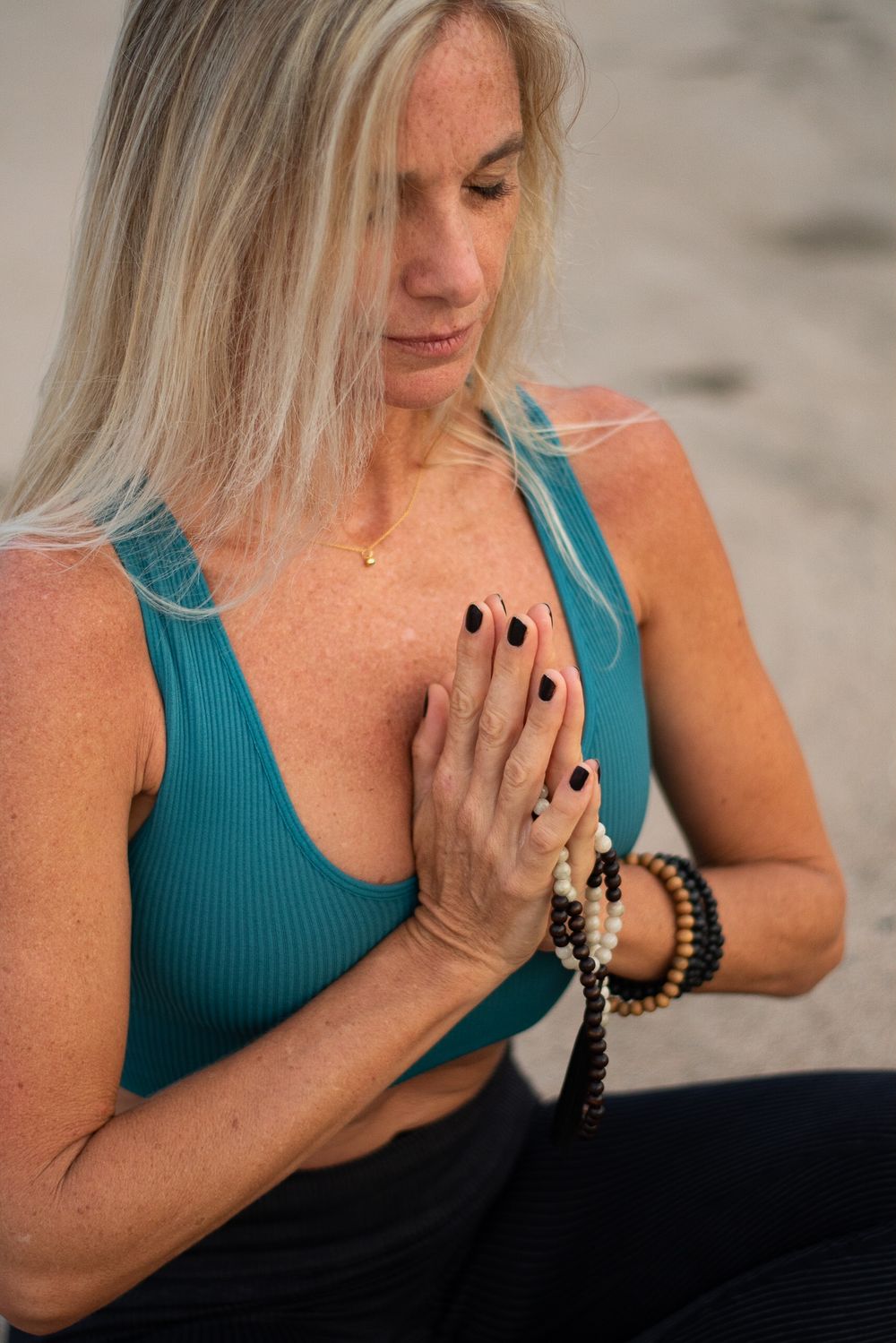 Person practicing mindfulness with prayer beads on beach wearing turquoise top.