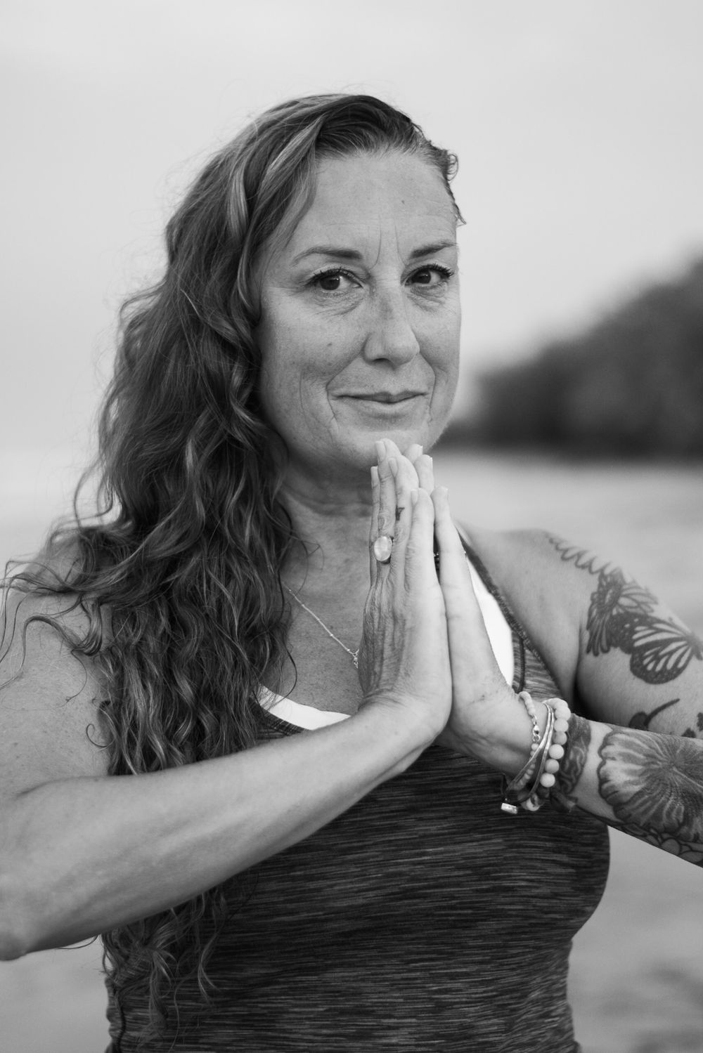 Black and white portrait of person in prayer pose wearing athletic wear on beach.