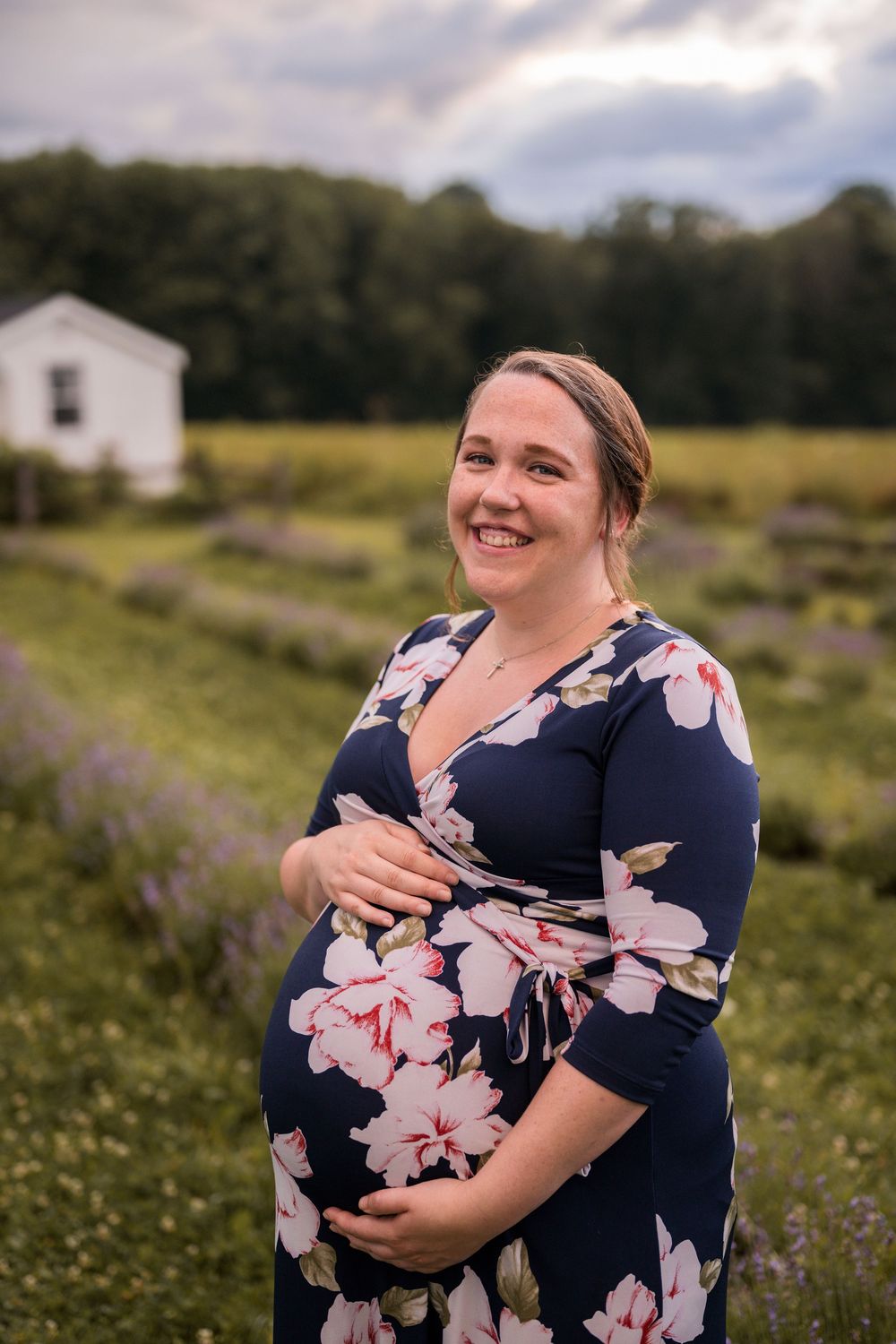 A person wearing a navy floral dress stands in a wildflower field during a golden hour photo session.