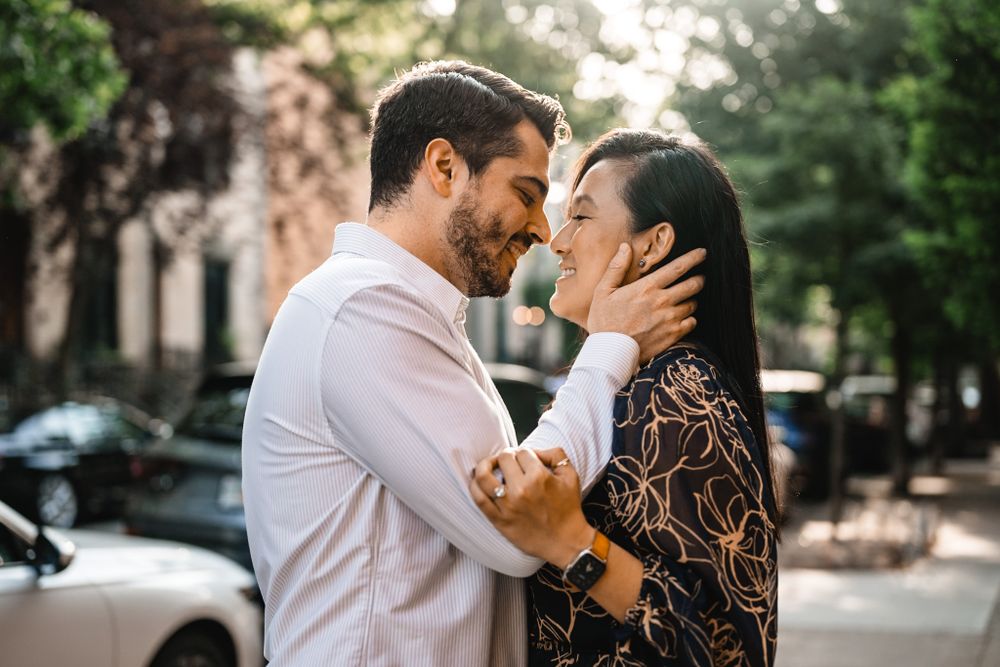 A couple embraces during a sunny outdoor photoshoot on a tree-lined street.