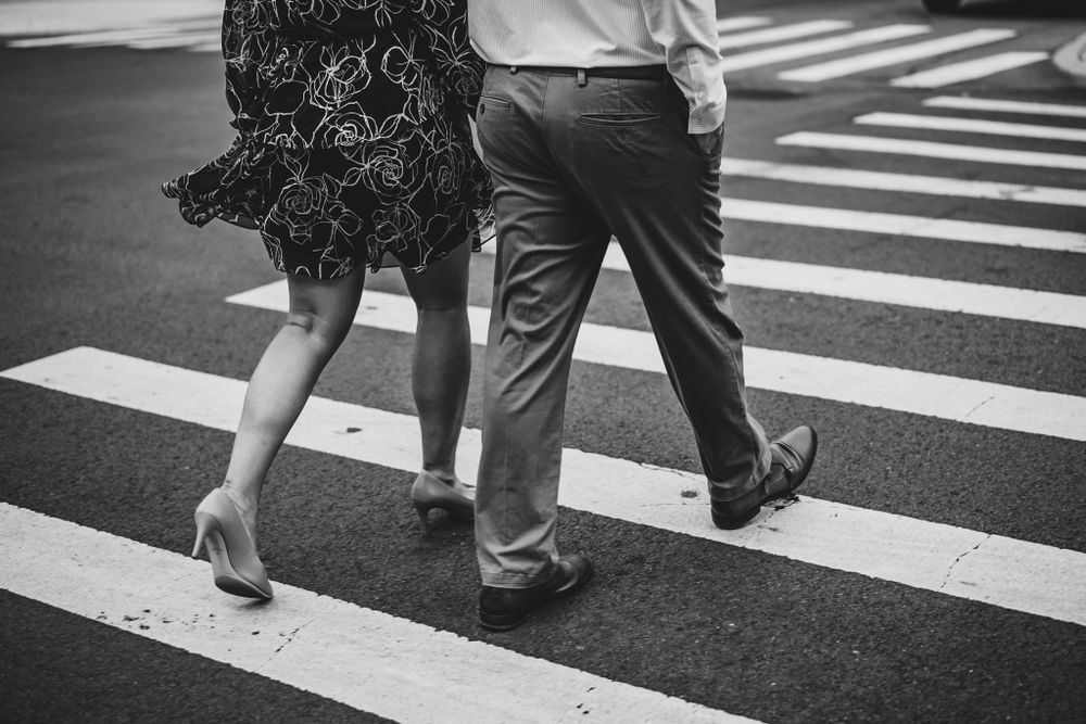 Close-up view of feet walking across an urban crosswalk in black and white.