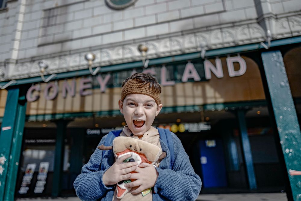 Excited child wearing a blue coat holds a small furry animal outside a storefront.