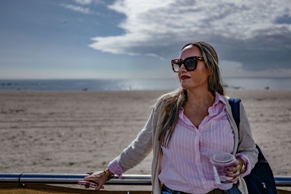 Woman in sunglasses and striped shirt enjoying view at sandy beach on sunny day.