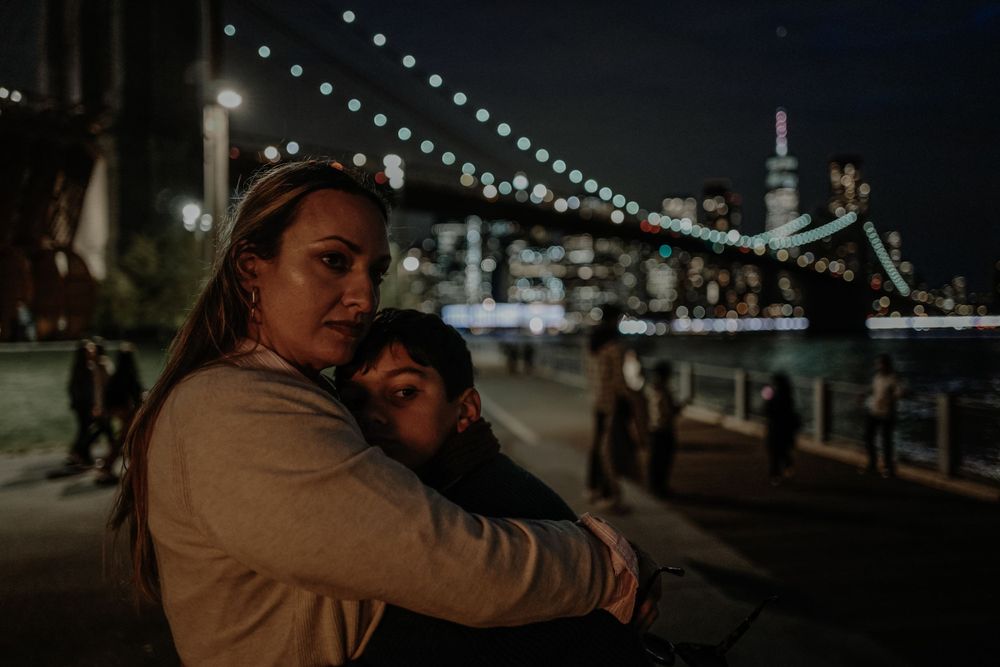 Nighttime view of illuminated Brooklyn Bridge with couple embracing in foreground.