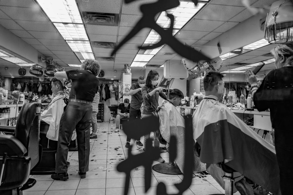 Black and white image of busy barber shop interior with multiple customers getting haircuts.