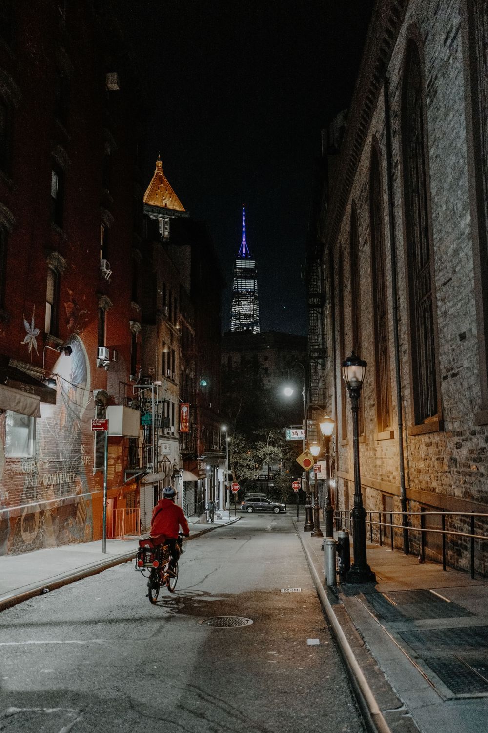 Person cycling down dark urban street with Empire State Building visible in background.