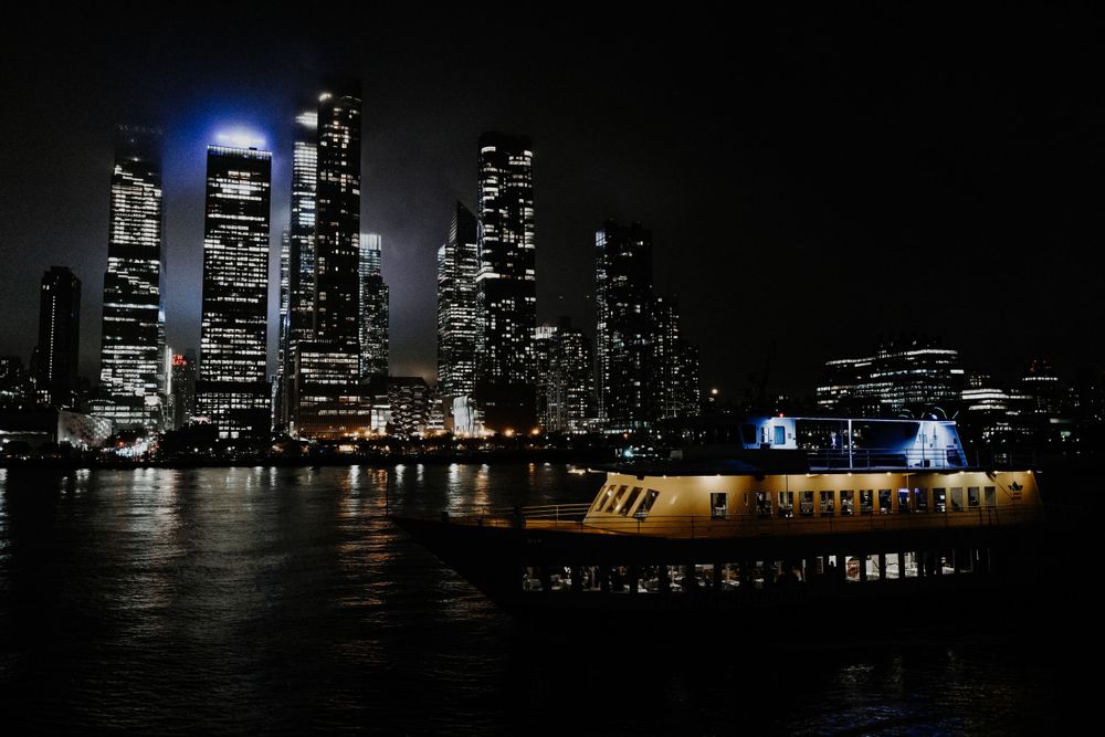 Illuminated skyline at night with ferry boat passing on dark water.