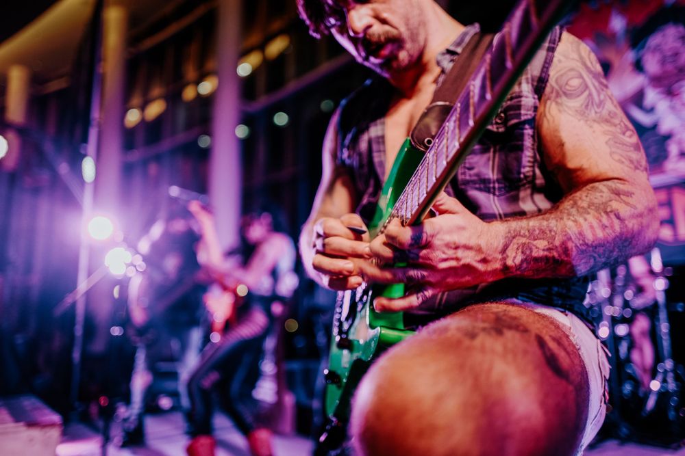 Musician playing electric guitar on stage with colorful concert lighting.