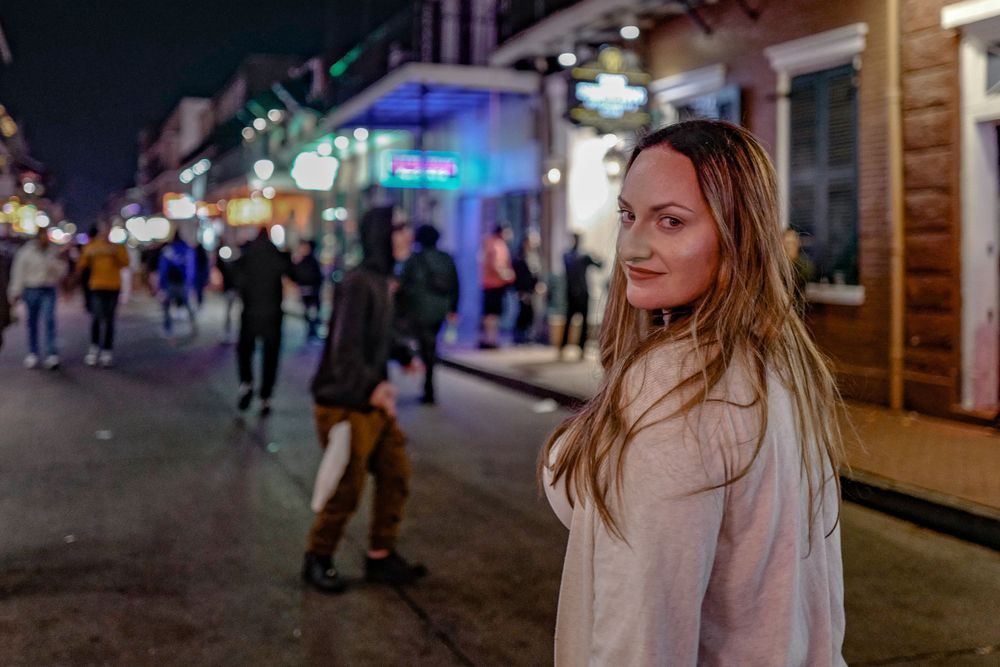 Nightlife scene on a lively street with neon lights and pedestrians walking past storefronts.